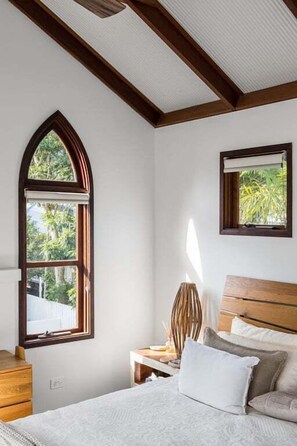 Un dormitorio con una cama grande, una mesita de noche, una lámpara y una ventana con vistas a zonas verdes.
