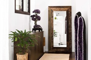 Un pasillo con un armario de madera, una planta en maceta, un espejo y una puerta que da al baño.