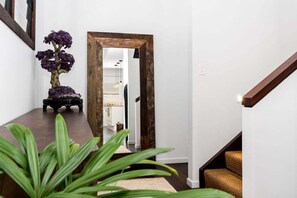 Un pasillo con puerta de madera, una planta en maceta y una escalera.