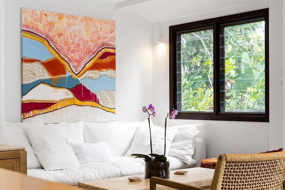 A room with a white sofa, a wooden table, and a large abstract painting on the wall.