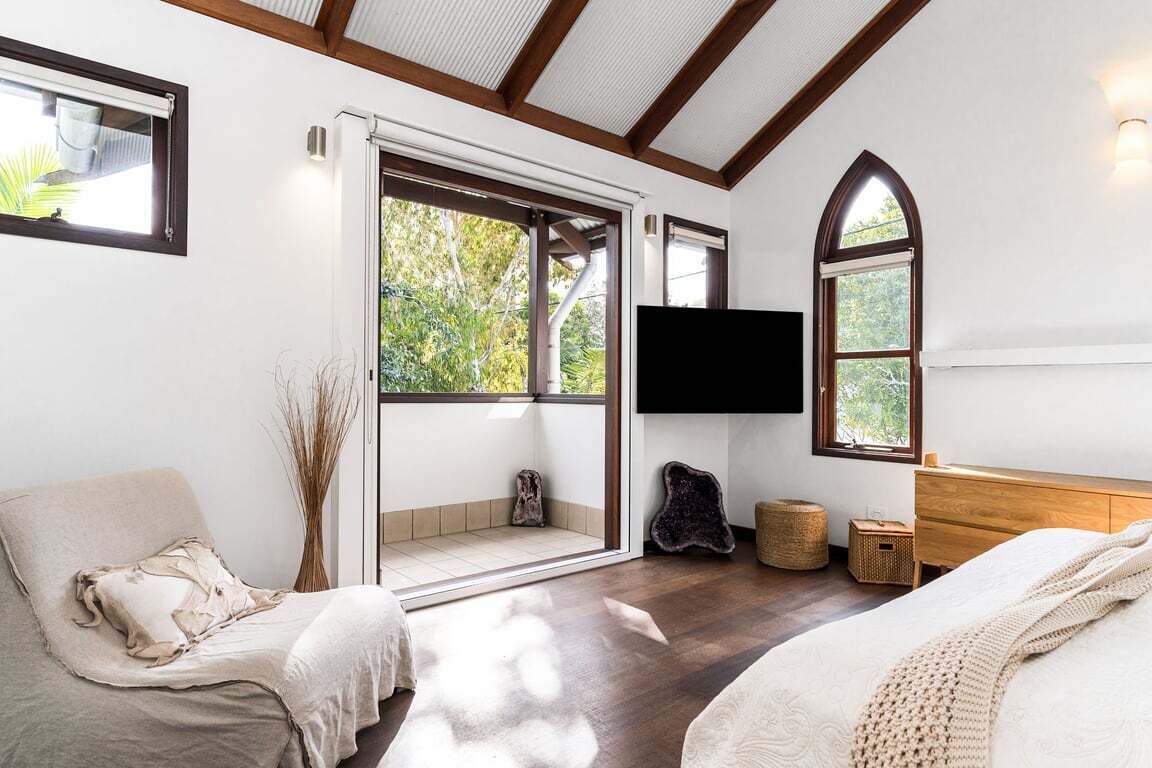 A bedroom with a large window, a flat-screen TV, a bed, a sofa, and a wooden dresser.