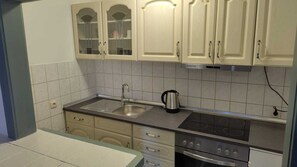 A kitchen with a stainless steel sink, a kettle, and a stove.