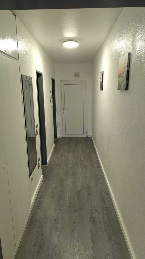 A hallway with a door at the end, a light fixture on the ceiling, and a small picture on the wall.