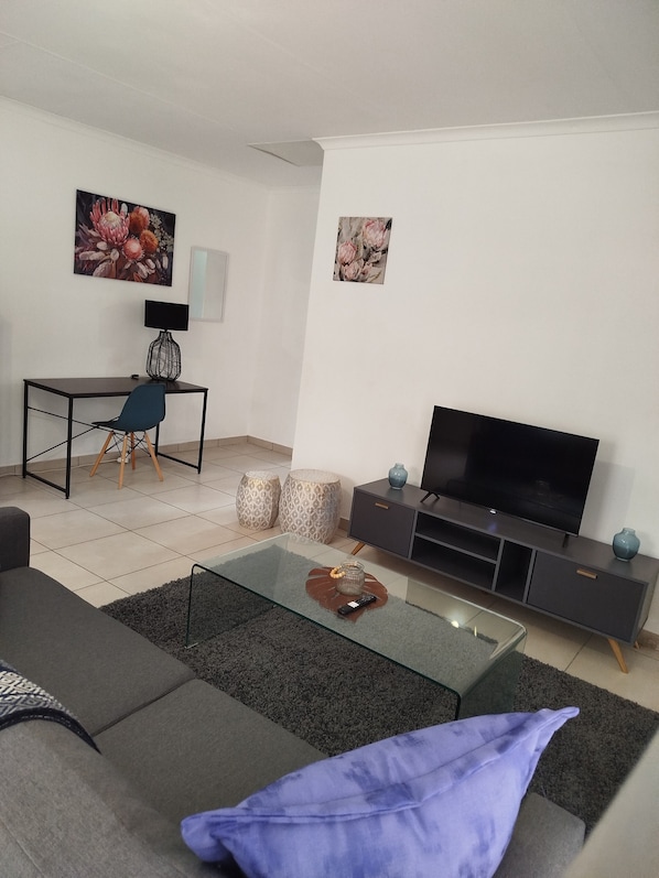 A modern living room with a sofa, coffee table, TV, and a desk with a chair.