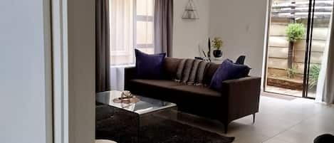 A modern living room with a sofa, coffee table, and two patterned ottomans.