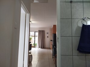 A hallway leading to a kitchen with a refrigerator, a sink, and a window with curtains.