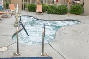 Ein Whirlpool mit Schild ‚Nicht Springen‘, umgeben von Liegestühlen und einem Zaun.