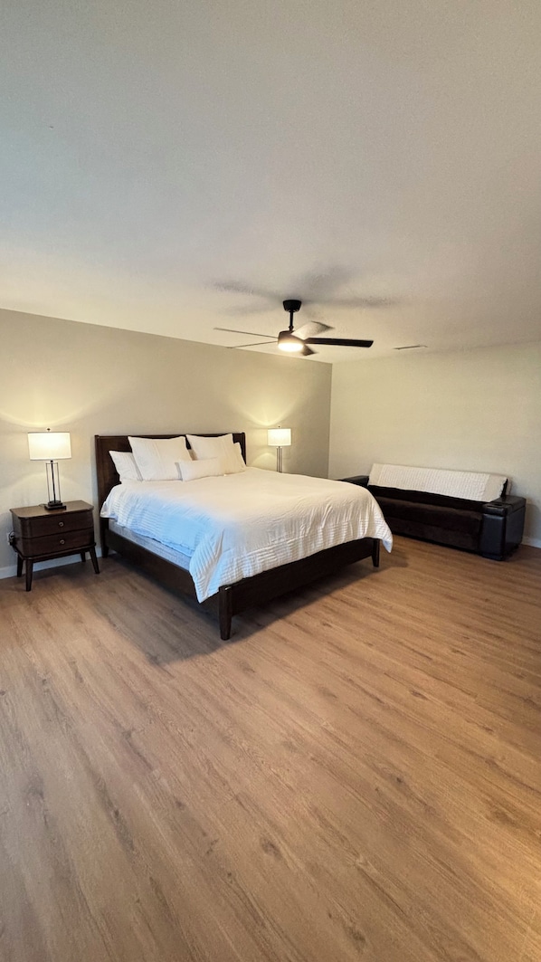 A bedroom with a bed, two bedside tables, a ceiling fan, and a bench.