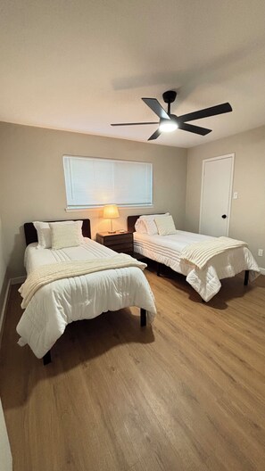 A bedroom with two beds, a ceiling fan, a window with blinds, and a door. - Cozy Katy Home near Katy Mills, Restaurants, and Family Attractions (Katy)