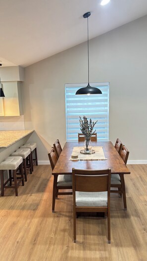 A dining area with a wooden table, six chairs, a vase with flowers, and a pendant light. - Cozy Katy Home near Katy Mills, Restaurants, and Family Attractions (Katy)