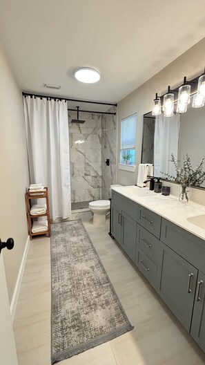 Une salle de bain moderne équipée d’une douche, de toilettes, d’un meuble-lavabo et d’un grand miroir.