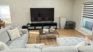A modern living room with a sectional sofa, a coffee table, a flat-screen TV, and a ceiling fan. - Cozy Katy Home near Katy Mills, Restaurants, and Family Attractions (Katy)