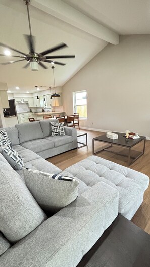 A modern living room with a sectional sofa, a coffee table, and a ceiling fan. - Cozy Katy Home near Katy Mills, Restaurants, and Family Attractions (Katy)