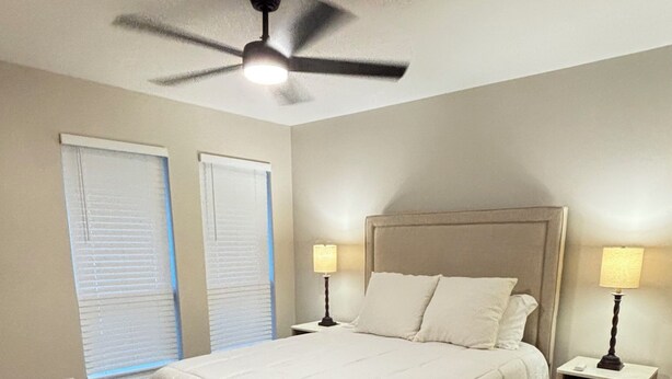 A bedroom with a bed, a ceiling fan, two bedside lamps, a nightstand, and a window with blinds. - Cozy Katy Home near Katy Mills, Restaurants, and Family Attractions (Katy)
