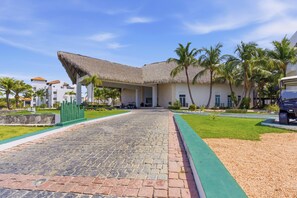A resort with a paved walkway leading to a building with a thatched roof. - Luxury Beachfront Penthouse Punta Palmera Cap Cana (Punta Cana)