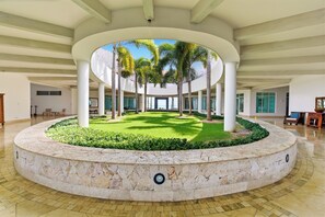 A circular courtyard with a central lawn, surrounded by palm trees and a stone wall. - Luxury Beachfront Penthouse Punta Palmera Cap Cana (Punta Cana)