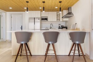Een moderne keuken met een centraal kookeiland, roestvrijstalen apparatuur en drie barkrukken.