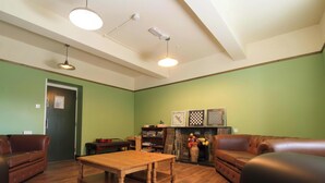 A living room with green walls, a wooden table, two leather sofas, a fireplace, and a bookshelf.