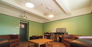 A living room with green walls, a wooden table, two leather sofas, a fireplace, and a bookshelf.