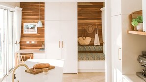 A modern kitchen with white cabinetry, a wooden accent wall, a built-in bench, and a coffee machine. - Casa Collection Bicheno- Casa Original (Bicheno)