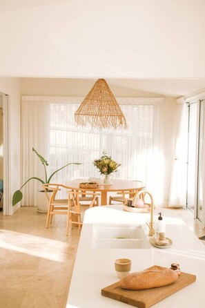 A bright room with a dining table, chairs, a hanging light fixture, and a large window.