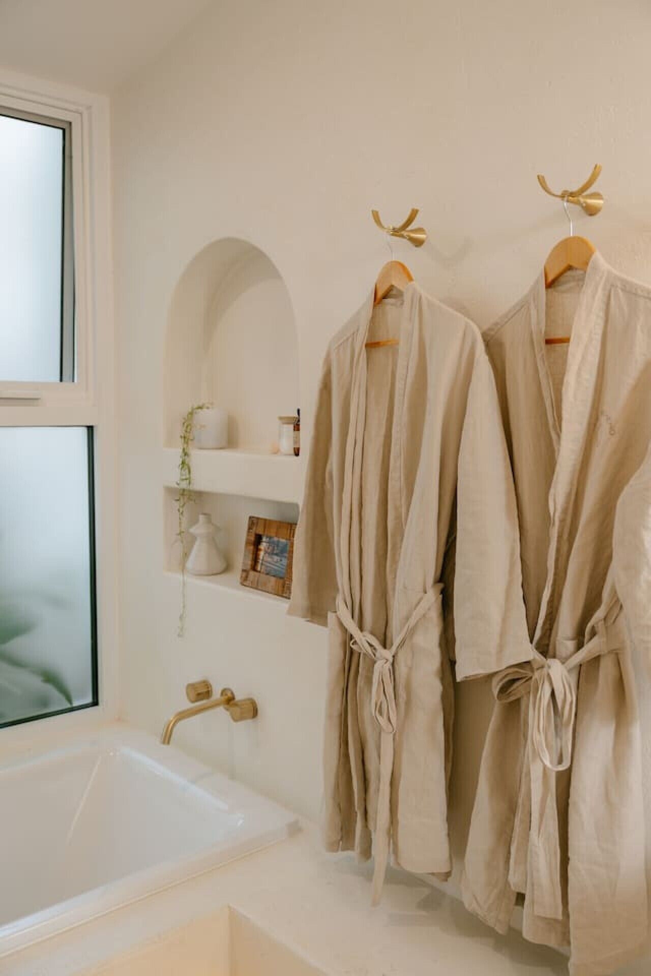 A bathroom with a bathtub, two robes hanging on a rack, and a shelf with decorative items.