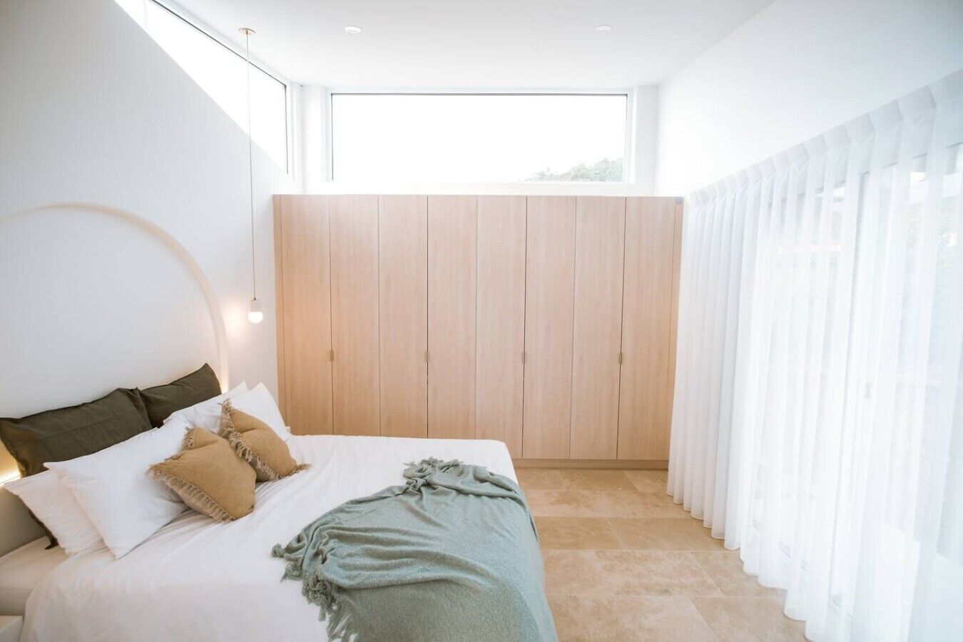 A modern bedroom with a bed, wooden wardrobe, and sheer curtains.