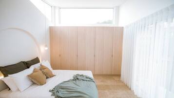 A modern bedroom with a bed, wooden wardrobe, and sheer curtains.