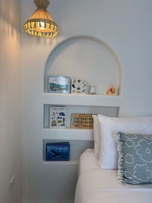 Ein Zimmer mit einem weißen Bett, einer Lampe und Regalen mit Büchern und Dekoartikeln.