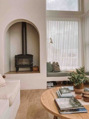Ein Wohnzimmer mit Kamin, einer Couch, einem Fenster mit Vorhängen und einem Couchtisch mit Büchern.