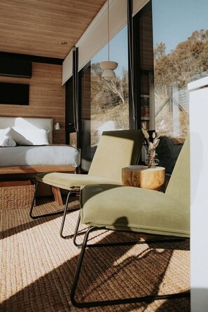 Ein modernes Schlafzimmer mit einem Bett, einer Sitzecke mit Sessel und Beistelltisch sowie einem großen Fenster mit Blick ins Freie.