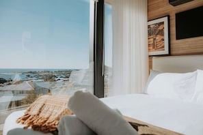 Ein Hotelzimmer mit großem Fenster, einem Bett mit weißer Bettwäsche, einem Holzkopfstück und einem gerahmten Bild an der Wand.