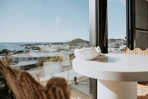 A room with a view of a coastal town, a round table, and a wicker chair. - Casa Collection Bicheno ~ The Bambino (Bicheno)