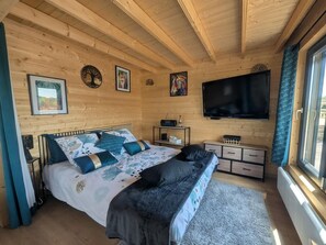 Ein Schlafzimmer mit Holzwänden, einem Bett, einem Fernseher und Kunstwerken an den Wänden.