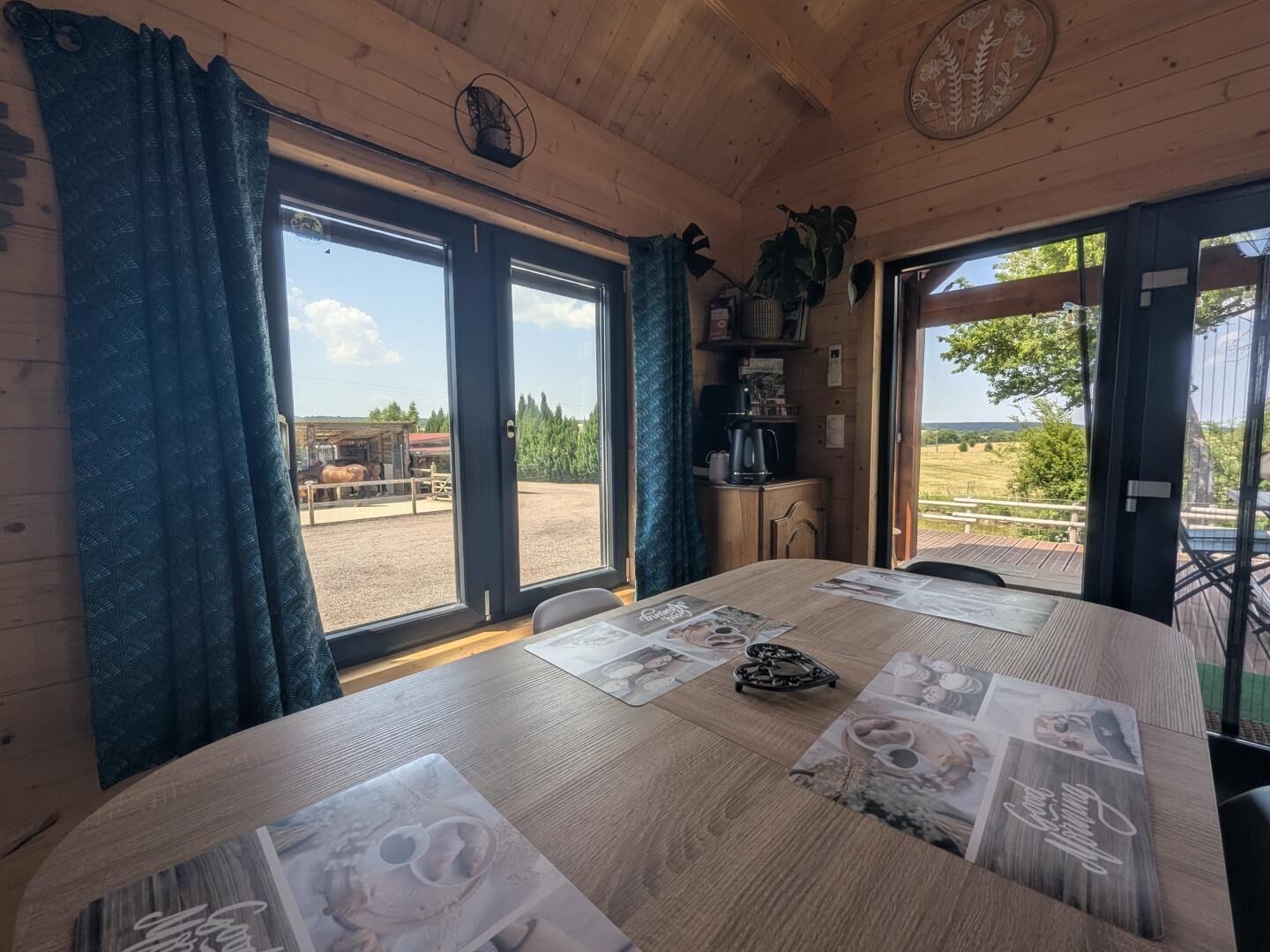 Un intérieur en bois avec une table à manger dressée pour quatre personnes, de grandes fenêtres et une vue sur l’extérieur.