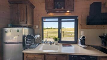 Cocina con armarios de madera, un refrigerador de acero inoxidable, un lavavajillas Bosch y una ventana con vistas a un campo.
