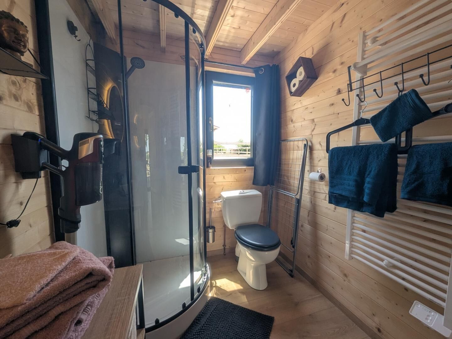 A compact bathroom with a glass shower enclosure, a toilet, and a towel rack with folded towels.