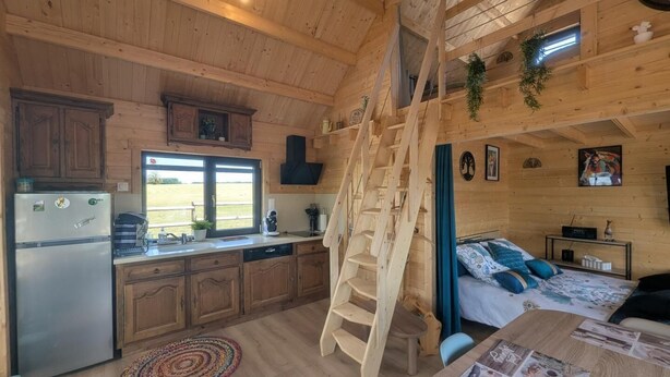 Interior de una cabaña con cocina, comedor y dormitorio en un altillo.