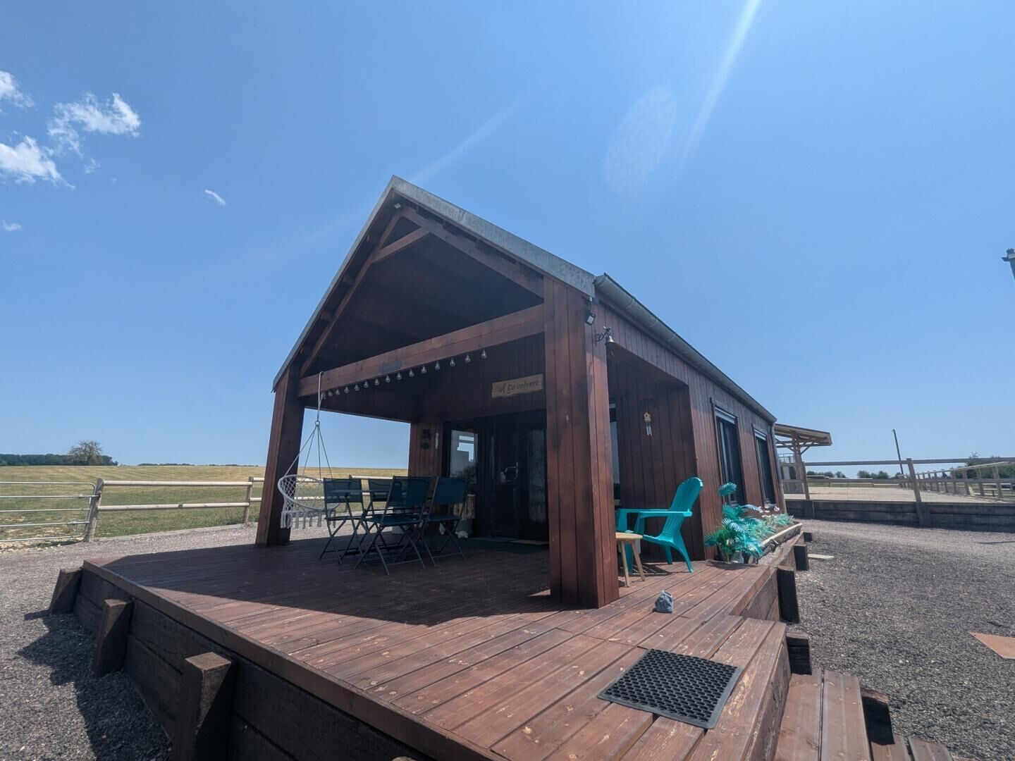 A wooden building with a covered porch, outdoor seating, and a gravel ground.