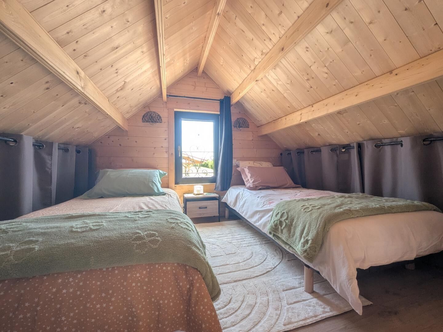 A cozy attic bedroom with two beds, a window, and a small table.