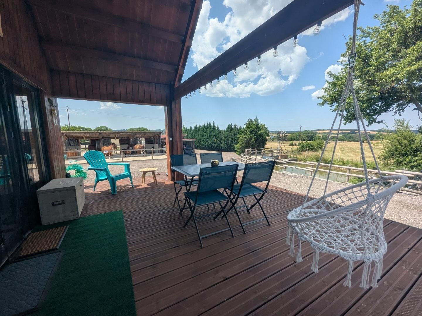 Eine Terrasse im Freien mit Tisch und Stühlen, einem Hängesessel und Blick auf eine Scheune mit Pferden.