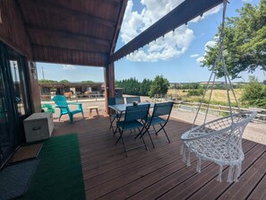 Eine Terrasse im Freien mit Tisch und Stühlen, einem Hängesessel und Blick auf eine Scheune mit Pferden.