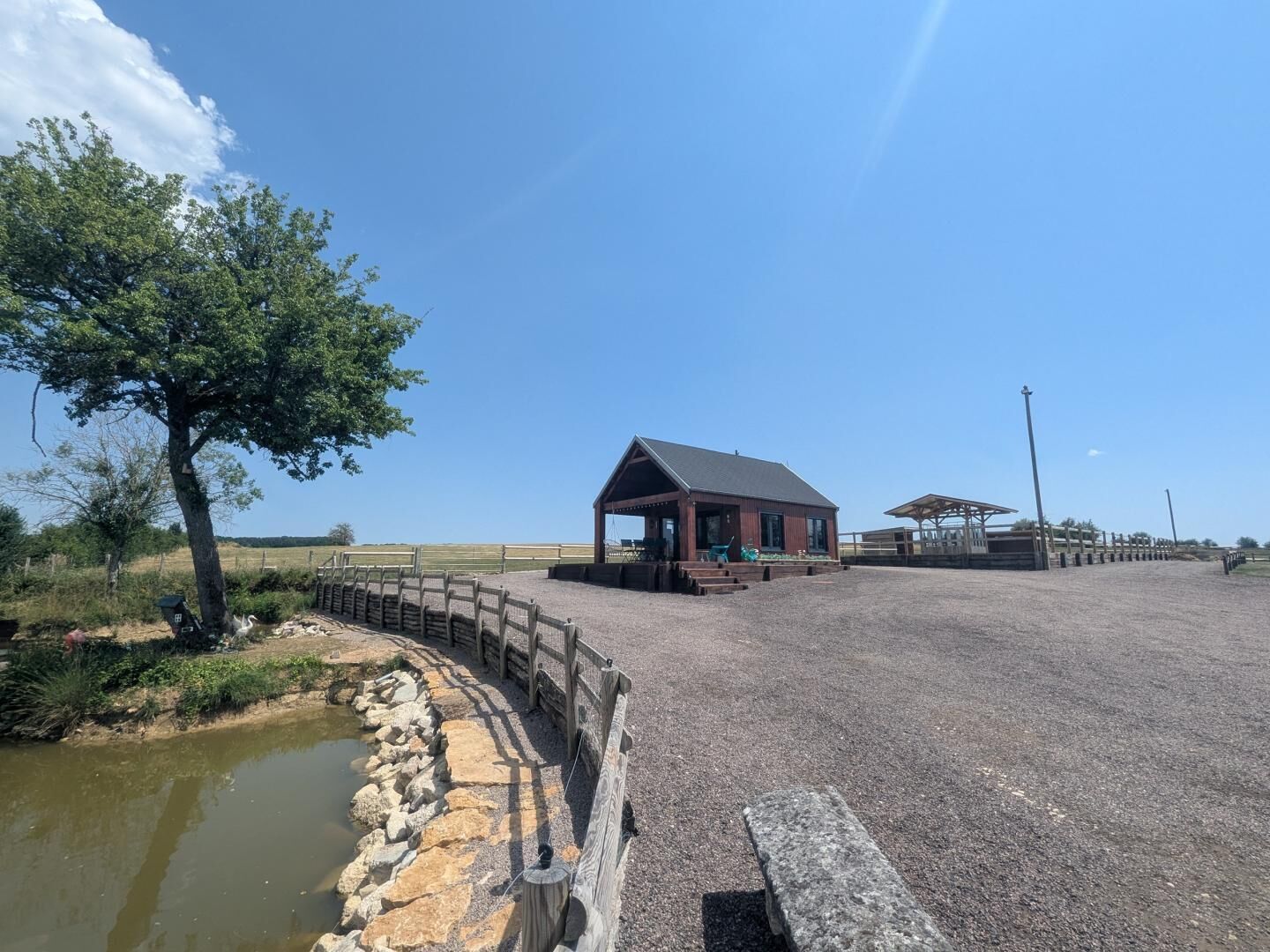 A stable with a covered area, a fenced paddock, and a small pond.