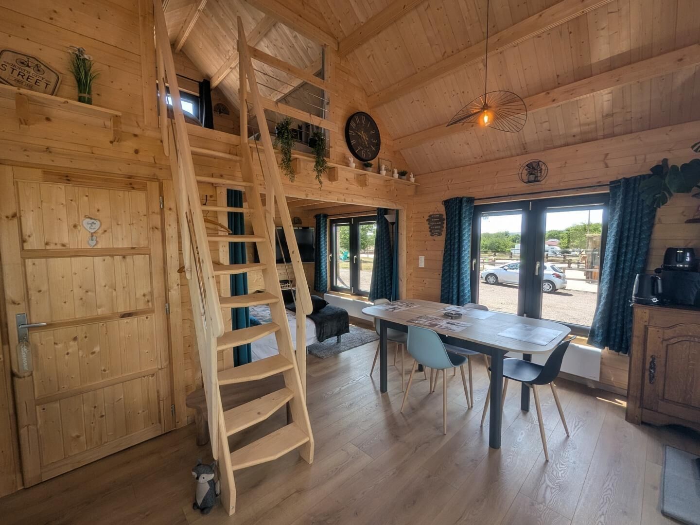 A wooden interior with a dining area, a staircase, and a view through the door.