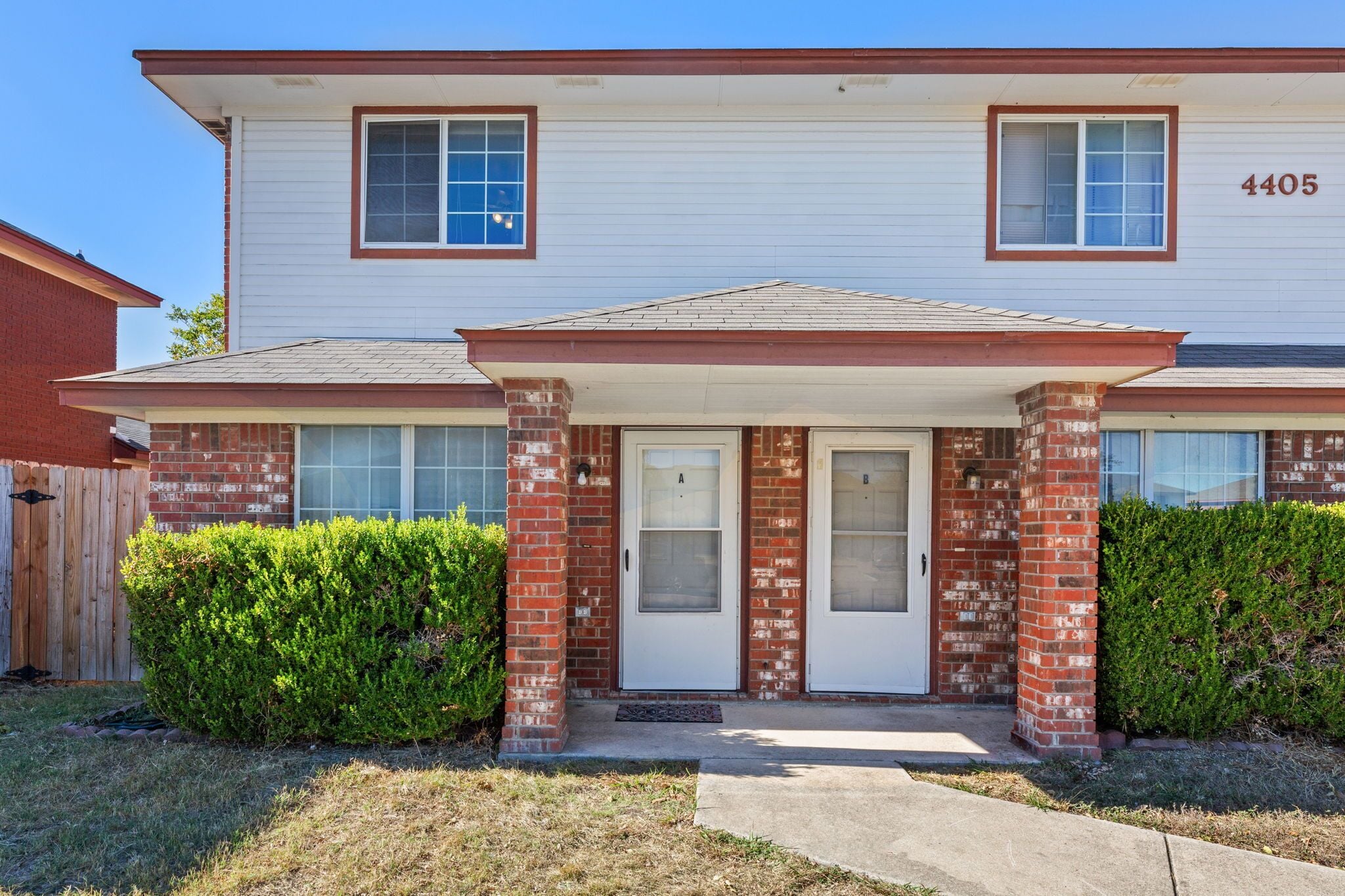 A two-story residential building with a front porch, a brick facade, and a garage door.