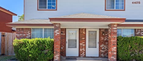 A two-story residential building with a front porch, a brick facade, and a garage door.
