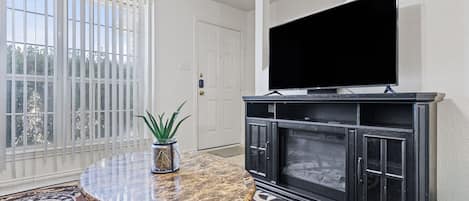 A living room with a television on a black cabinet, a round marble table with a plant, and a patterned rug.