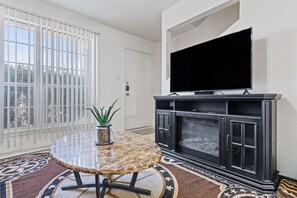 A living room with a television on a black cabinet, a round marble table with a plant, and a patterned rug.