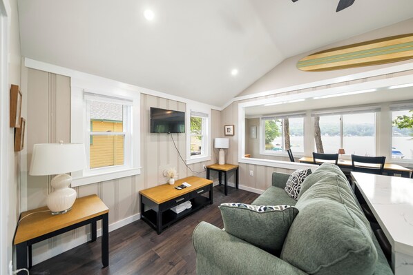 A modern living room with a sofa, a coffee table, a TV, and a dining area with a table and chairs. - Cabin 41 at The Historic Sandy Point Resort w/ Boat Slip and Onsite Boat ramp (Alton)