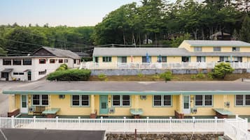 Um motel com uma fileira de quartos, cada um com varanda frontal e uma mesa pequena.